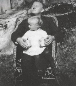 Fotografi av Gustav Vigeland sitter på Inga Syvertsens hytte ved Glomma i Varteig  i Østfold med hennes niese Irene på fanget